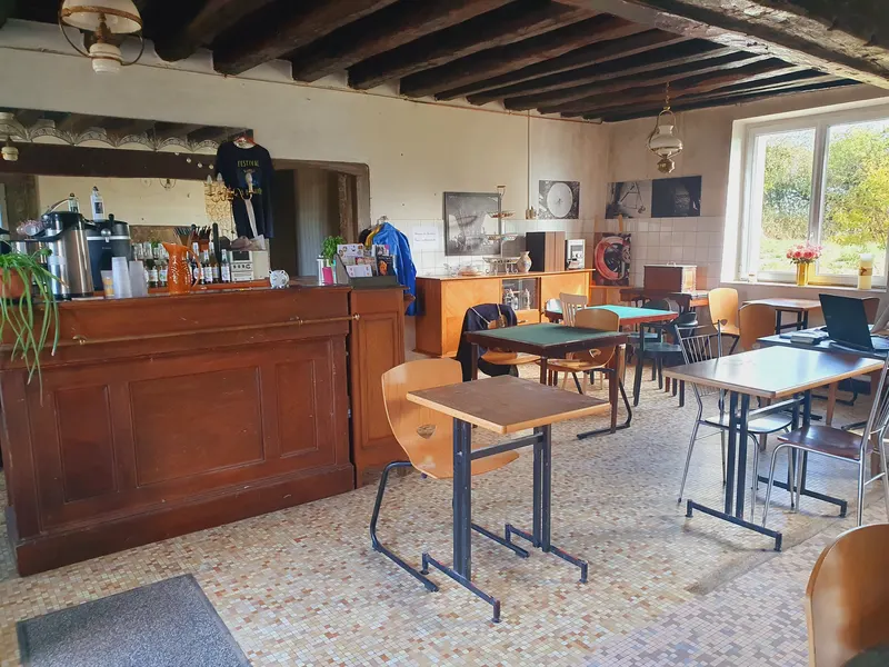 Le comptoir en bois du café, les tables et le carrelage ancien sous les poutres.