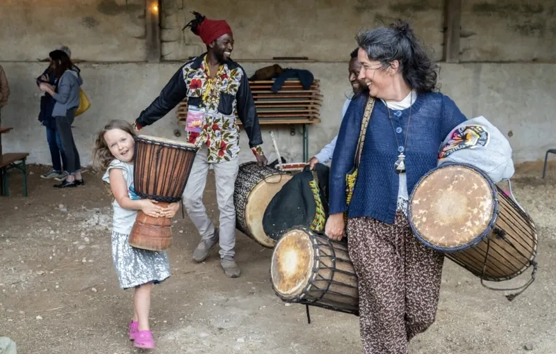 Une enfant, un musicien et une femme portent de grands djembés.