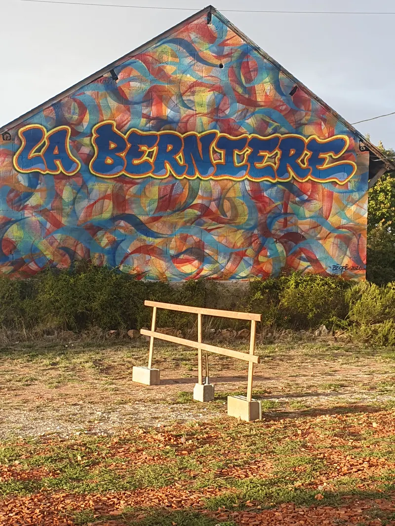 Le pignon de la grange peint d'arabesques bleues, roses et jaunes, avec le nom La Bernière en grandes lettres.