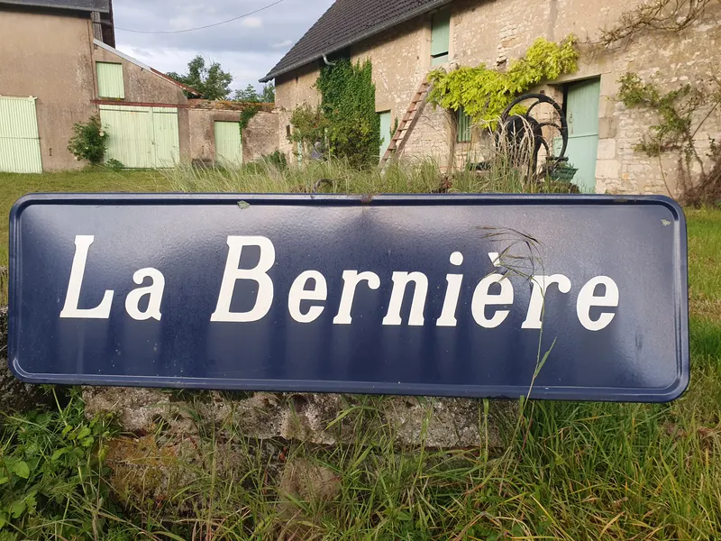 La plaque émaillée bleue La Bernière posée dans l'herbe devant la longère.