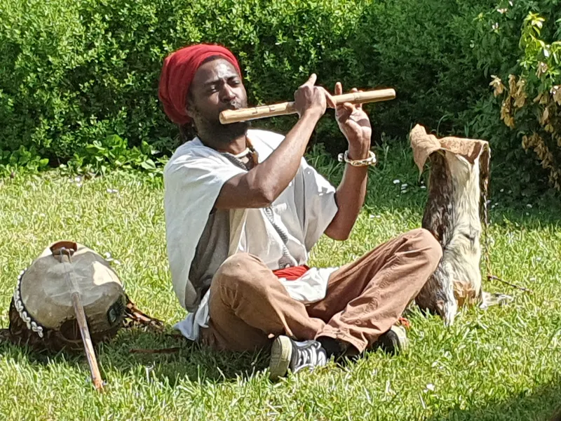 Yomba assis dans l'herbe joue d'une flûte en bois.